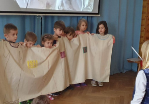 Dzieci stoją - jako chór w operze śpiewają, a dziewczynka dyryguje.