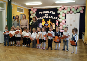 Pasowanie na Przedszkolaka grupy Sówek. Dzieci w półkolu stoją i trzymają dyplomy.