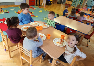 Dzieci siedzą przy stolikach i podziwiają własnoręcznie przygotowane pizzę z okazji Światowego Dnia Pizzy.
