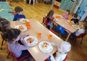 Dzieci siedzą przy stolikach i podziwiają własnoręcznie przygotowane pizzę z okazji Światowego Dnia Pizzy.