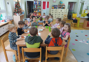 Dzieci siedzą przy stolikach i jedzą własnoręcznie przygotowane przez siebie pizze z okazji Światowego Dnia Pizzy.