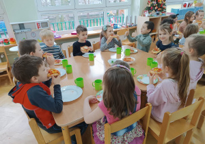 Dzieci siedzą przy stolikach i jedzą własnoręcznie przygotowane przez siebie pizze z okazji Światowego Dnia Pizzy.