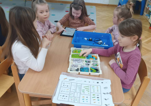 Dziewczynki siedzą przy stoliku i próbują złożyć robota z klocków lego na zajęciach z robotyki.