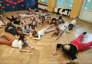 Dzieci wspólnie z trenerką zumby odpoczywają na podłodze po tańcu.