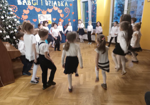 Dzieci ustawione w kole wykonują taniec podczas występu dla babć i dziadków z okazji ich święta.