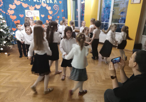 Dzieci elegancko ubrane tańczą w parach podczas występu dla dziadków.