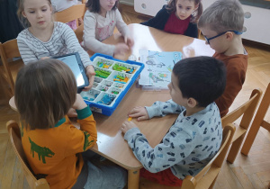 Dzieci siedzą przy stoliku próbują złożyć robota z klocków lego na zajęciach z robotyki.