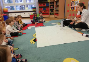 Dzieci siedzą na dywanie, a prowadząca warsztaty LABOLO wyjaśnia im, o co chodzi z ciśnieniem.