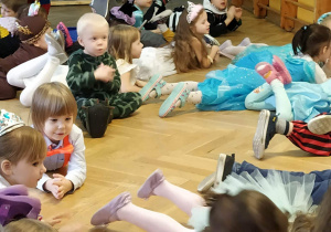 Dzieci przebrane w różne stroje leżą na podłodze podczas balu karnawałowego.