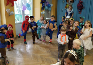 Dzieci tańczą podczas balu karnawałowego z jedną nogą podniesioną do góry.