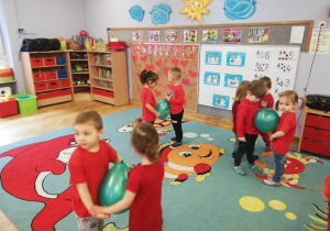 Dzieci ubrane na czerwono ustawione w pary tańczą z balonami między brzuszkami.