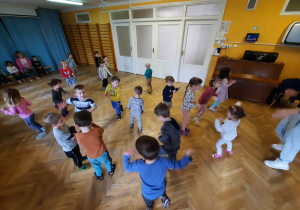 Dzieci w rozsypce na sali gimnastycznej tańczą dowolnie do piosenki.