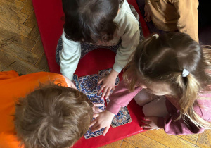 Dzieci siedzą na materacu i układają większy wzór z kafelków.
