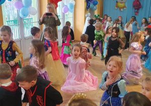 Dzieci przebrane w różne stroje tańczą do szybkiej piosenki podczas balu karnawałowego.