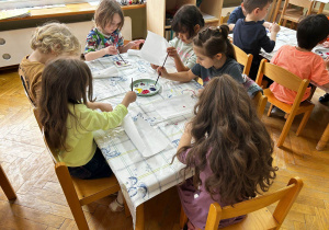 Dzieci siedzą przy stoliku i samodzielnie malują kolorowe wzorki na kafelkach.