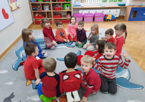 Dzieci ubrane na czerwono siedzą w kole przekazując sobie maskotkę wielkiego serduszka.
