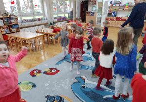 Dzieci ubrane na czerwono tańczą po kole do szybkiej muzyki.