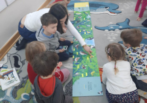 Akcja "Czytamy, głowy otwieramy", dzieci siedzą na dywanie i razem z mamą kolegi oglądają ilustracje w książeczce.
