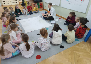 Dzieci siedzą w półkolu i słuchają prowadzącej warsztaty, która wyjaśnia im, o co chodzi z ciśnieniem.
