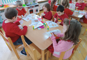 Dzieci siedzą przy stolikach i wycinają różne obrazki.