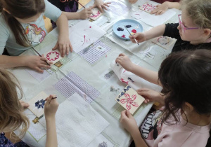 Dzieci siedzą przy stoliku i samodzielnie malują kolorowe wzorki na kafelkach.