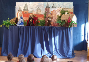Na scenie znajdują się kukiełki postaci występujących w przedstawieniu: król, królewna i dzielny rycerz.