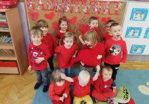 Dzieci ubrane na czerwono pozują do grupowego zdjęcia na tle napisu Walentynki.