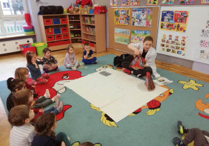Dzieci siedzą na dywanie i zapoznają się z wewnętrzną budową wulkanu przedstawioną na modelu.