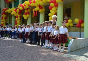 Starsze przedszkolaki stoją w rzędzię przed wejściem do budynku.