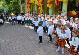 Dzieci ze wszystkich grup przedszkolnych stoją przed publicznością.