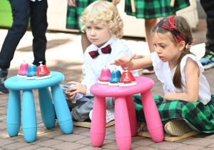 Dwoje dzieci siedzi i gra na dzwonkach.
